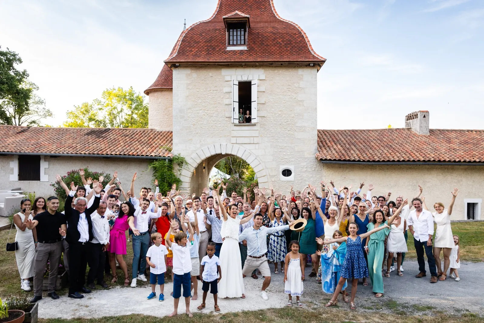 Les mariés entourés de tous leurs invités devant le château, les bras levés